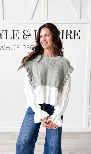 Woman wearing an olive sweater over a white shirt with blue jeans