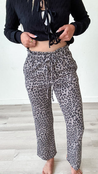 Person wearing a black cropped top and leopard print pants on a light wooden floor.