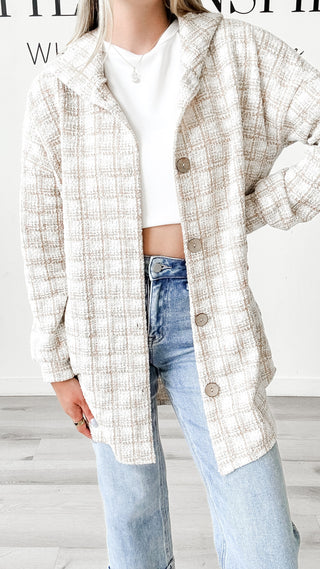 Person wearing a plaid shirt over a white top and jeans on a light wooden floor.