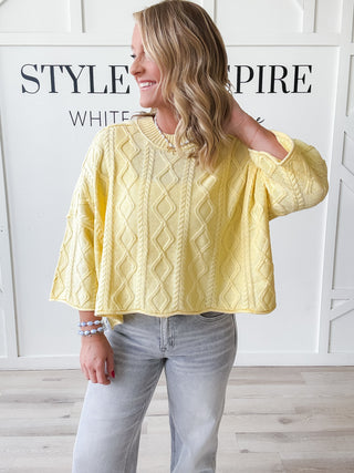 Woman wearing a cropped yellow cable knit sweater 