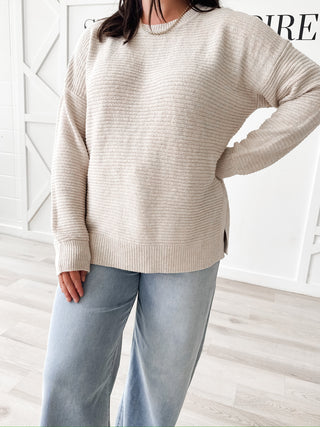 Person wearing a beige sweater and light blue jeans against a white background