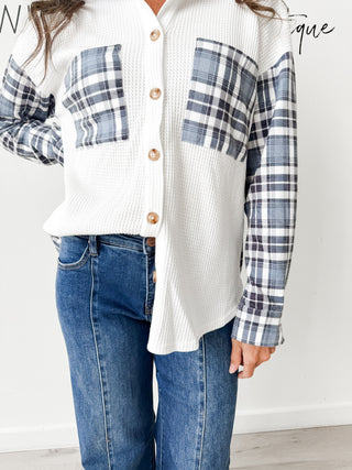 Person wearing a white shirt with plaid sleeves and blue jeans on a plain background
