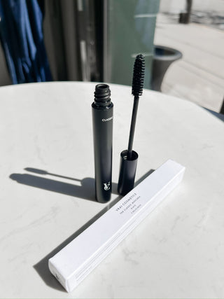 Black mascara with wand and packaging on a light surface