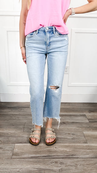 Woman wearing light blue cropped jeans with minimal distressing on left knee, and a raw hem. 