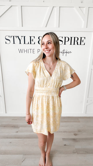 Woman wearing a light yellow v-neck dress with flutter sleeves
