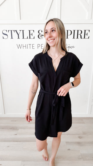 Woman wearing a black v-neck dress with a belt tie. 